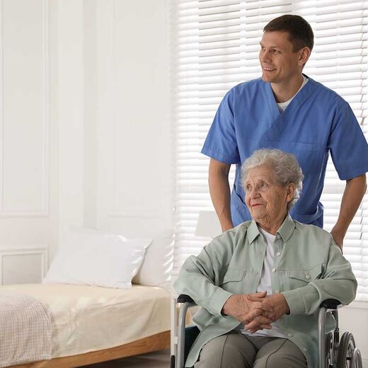 Seniorin im Rollstuhl wird von Pfleger geschoben