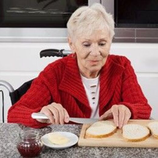 Ältere Dame schmiert sich ein Brot 