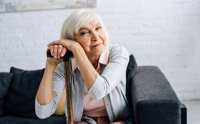 Seniorin sitzt auf der Couch und lehnt sich an ihren Gehstock © LIGHTFIELD STUDIOS - stock.adobe.com 30875968