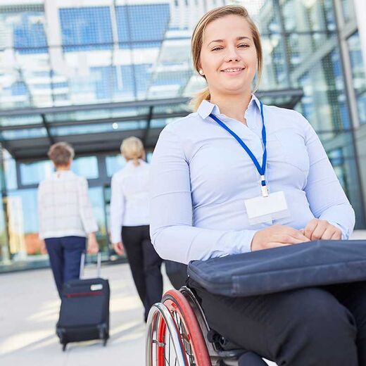 Frau im Business Outfit sitzt lächelnd im Rollstuhl