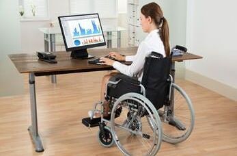 Zuschüsse für Menschen mit Behinderung: Eine Rollstuhlfahrerin sitzt an ihrem Platz und arbeitet am PC