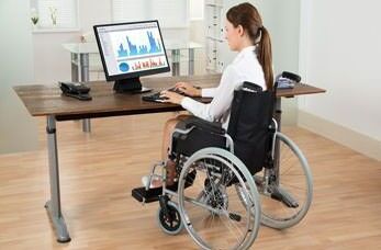 Behindertengerechter Arbeitsplatz: Eine Rollstuhlfahrerin sitzt an ihrem Platz und arbeitet am PC