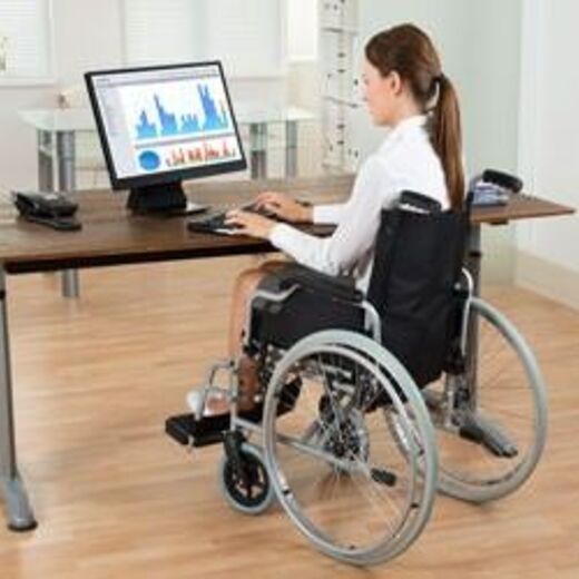 Behindertengerechter Arbeitsplatz: Eine Rollstuhlfahrerin sitzt an ihrem Platz und arbeitet am PC