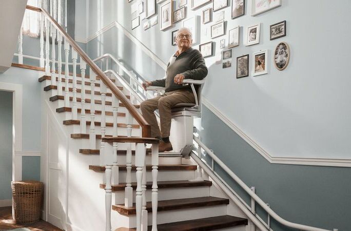 Senior fährt mit einem Treppenlift die Treppen in seinem Haus hoch. - 