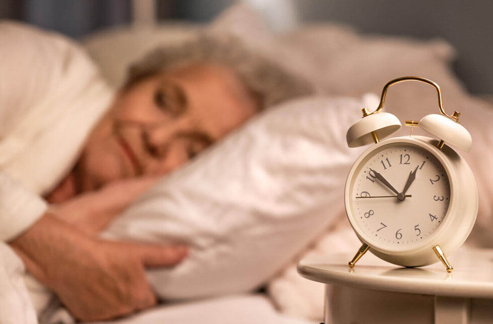 Wecker auf dem Nachttisch einer schlafenden Seniorin. © Pixel-Shot - stock.adobe.com