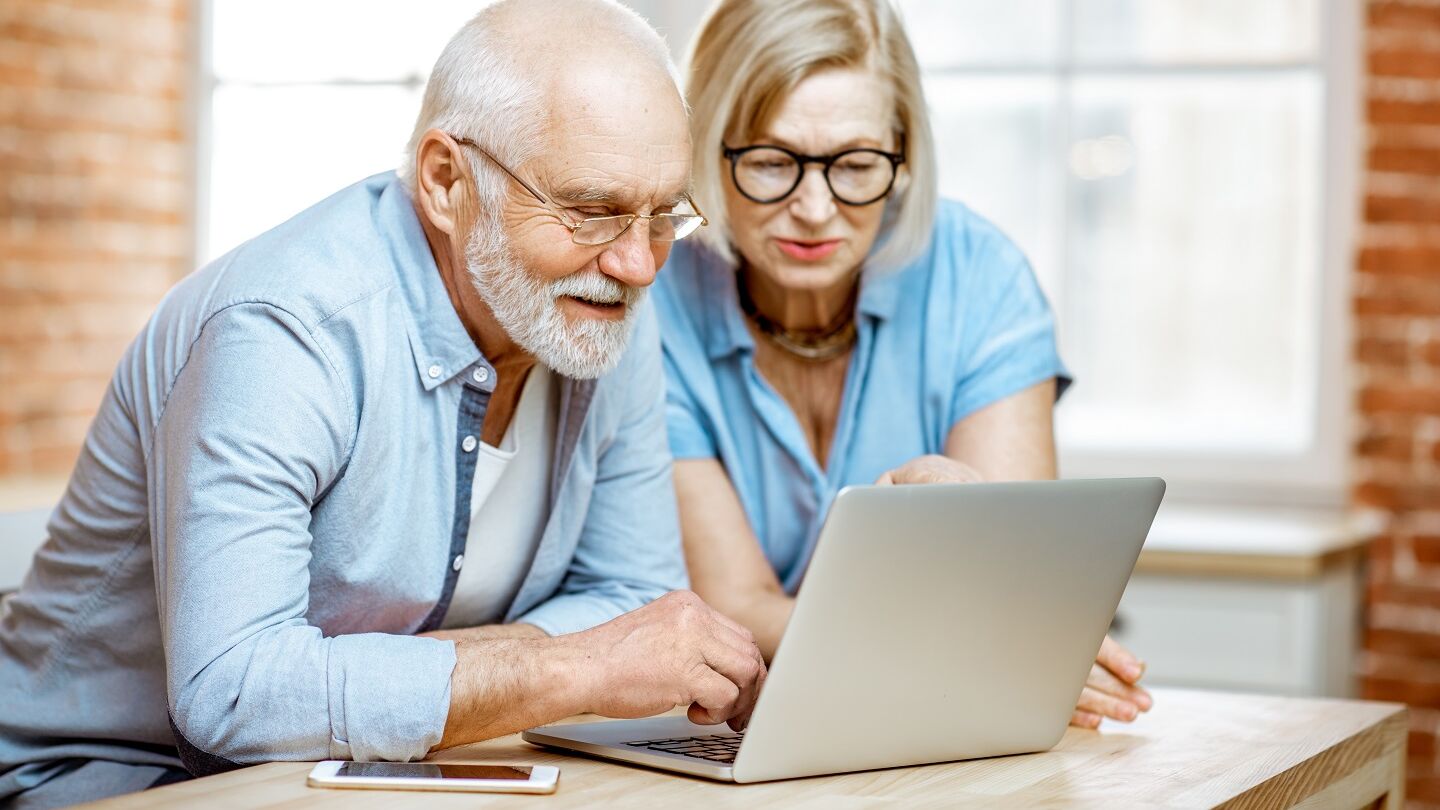 Ein Senior und seine Angehörige schauen auf einen Laptop zum Modellvergleich von Treppenliften