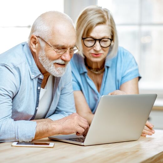 Ein Senior und seine Angehörige schauen auf einen Laptop zum Modellvergleich von Treppenliften