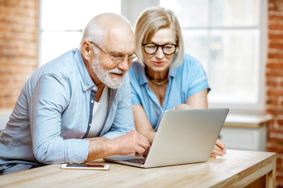 Ein Senior und seine Angehörige schauen auf einen Laptop zum Modellvergleich von Treppenliften