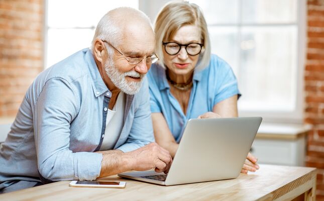 Ein Senior und seine Angehörige schauen auf einen Laptop zum Modellvergleich von Treppenliften