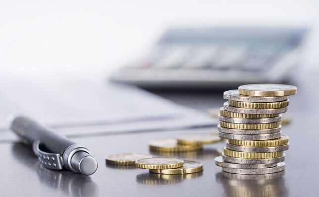 Kosten und Finanzierungen berechnen Münzen und einen Kugelschreiber auf einem Tisch