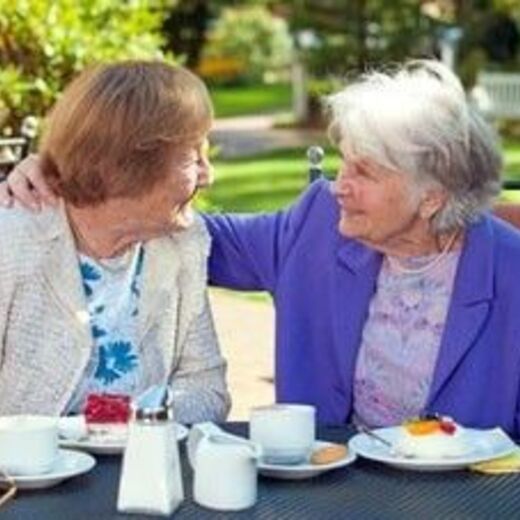 Zwei Seniorinnen sitzen bei Kaffee und Kuchen im Garten