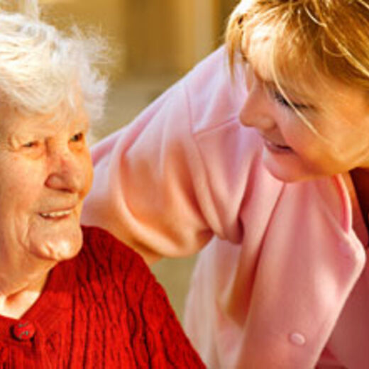Eine Seniorin lächelt ihre Pflegerin an