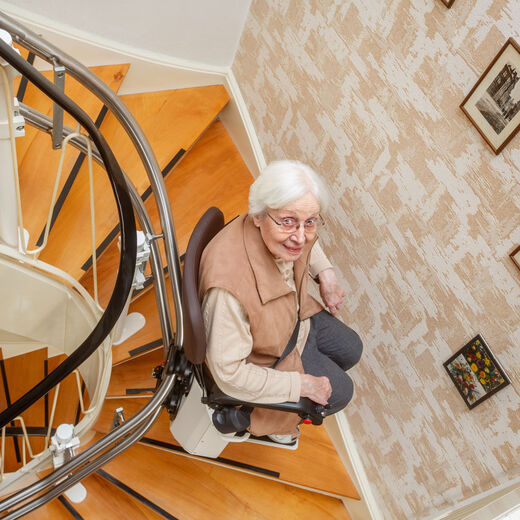 Seniorin fährt mit dem Treppenlift eine Wendeltreppe hoch