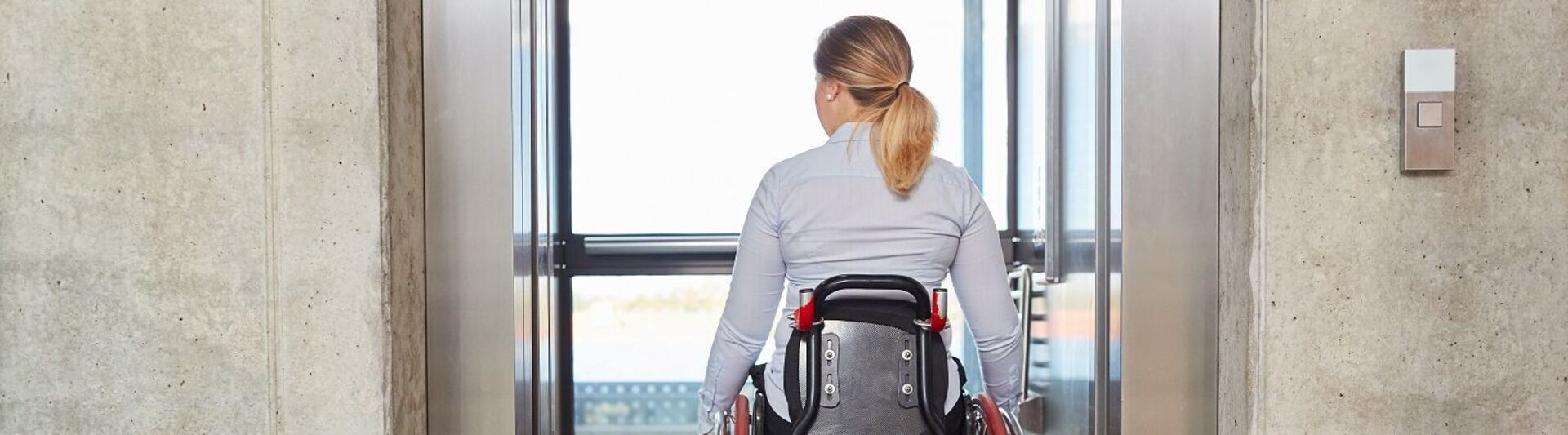 Frau fährt mit ihrem Rollstuhl in den Fahrstuhl