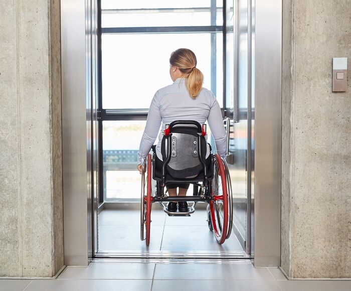 Frau fährt mit ihrem Rollstuhl in den Fahrstuhl