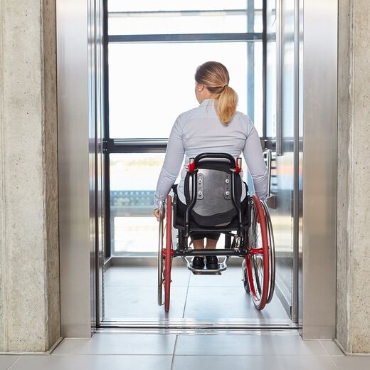 Frau fährt mit ihrem Rollstuhl in den Fahrstuhl