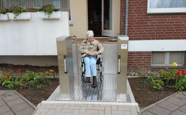 Ältere Dame im Rollstuhl auf einem Hublift im Außenbereich