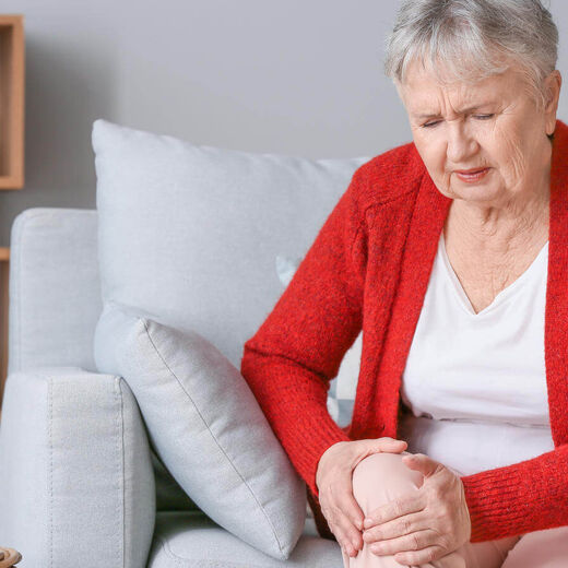 Seniorin sitzt auf der Couch und hält Ihr Knie fest, weil es schmerzt. © Pixel-Shot - stock.adobe.com