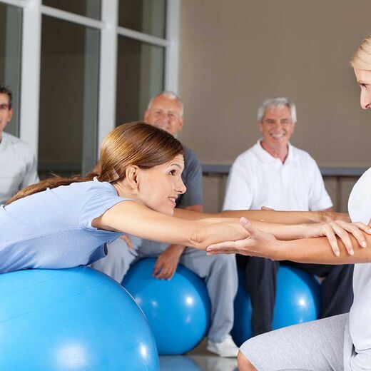 Zwei Senioren auf Gymnastikbällen mit einer Trainerin im Sportstudio