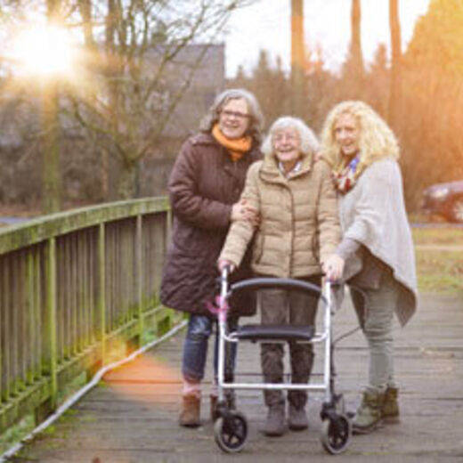 Eine Seniorin mit einem Rollator geht mit zwei Angehörigen spazieren