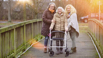 Eine Seniorin mit einem Rollator geht mit zwei Angehörigen spazieren