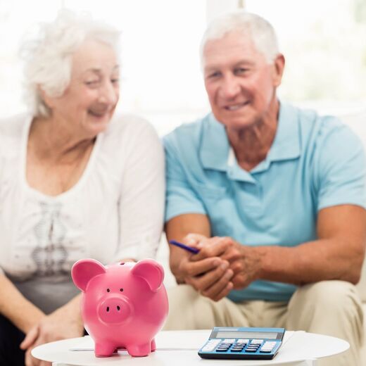 Zwei Senioren sitzen auf der Couch und schauen auf ein rosa Sparschwein