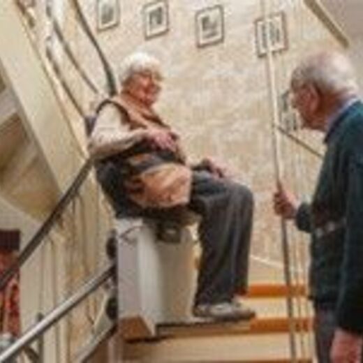 Seniorin fährt mit Sitzlift unter Beobachtung von ihrem Ehemann