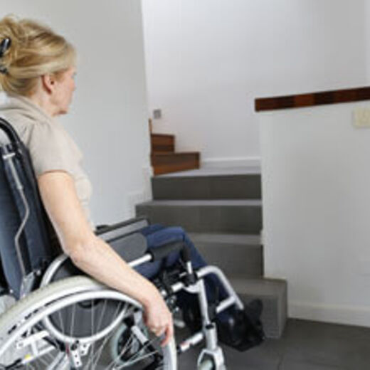 Frau im Rollstuhl steht vor einer Treppe