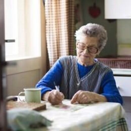 Seniorin sitzt am Küchentisch und schreibt