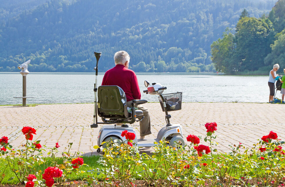 Renter in Rollstuhl schaut im Urlaub auf einen See