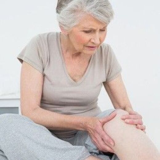 Knieschmerzen beim Treppensteigen: Eine Frau hält im Sitzen mit beiden Händen ihr linkes Knie fest