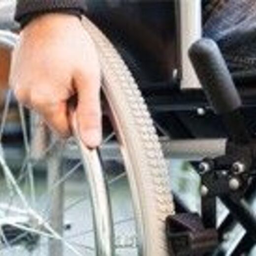 Eine Hand die das Rad vom Rollstuhl anschiebt