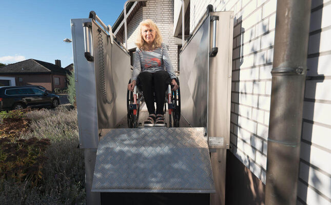 Rollstuhlfahrerin bewältigt Hauseingang mit Hublift. -