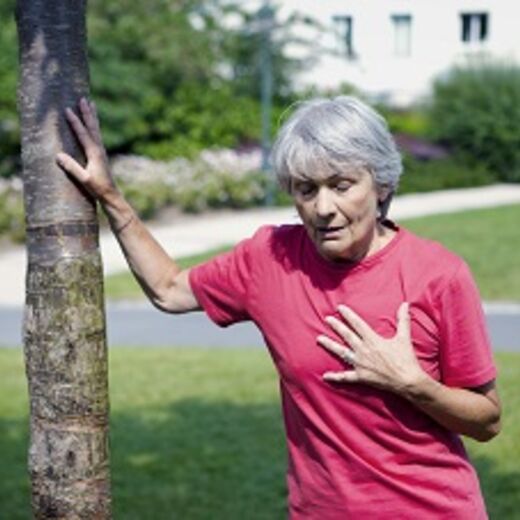 Eine Seniorin mit Atemnot hält sich den Brustkorb