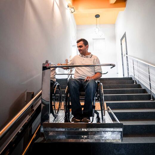 Mann im Rollstuhl fährt auf Plattformlift Treppe hinauf