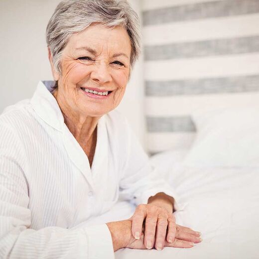 Seniorin kniet lächelnd am Bett