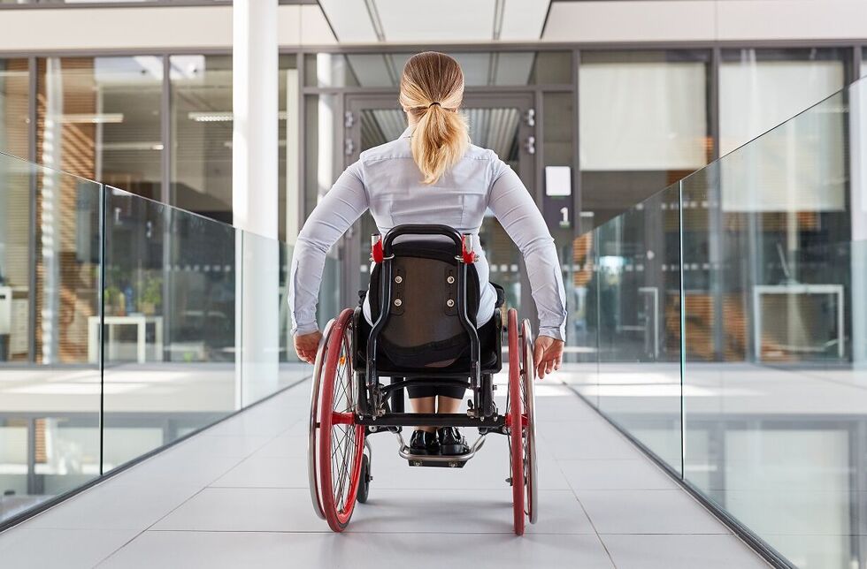 Frau fährt mit Rollstuhl durch den Büroflur