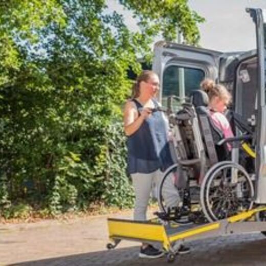 Rollstuhlfahrer fährt über eine Rampe in den Bus eines Fahrdienstes