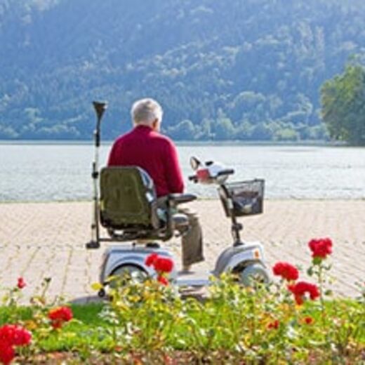 Senior auf dem Elektromobil schaut aufs Wasser hinaus