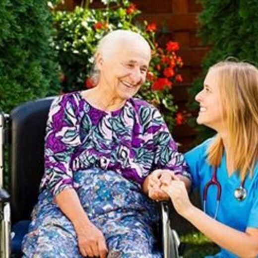 Seniorin sitzt im Rollstuhl und hält die Hand von der Pflegerin