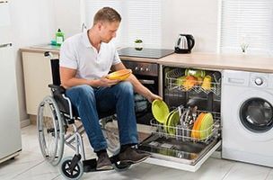 Rollstuhlfahrer räumt Spülmaschine in der Küche aus