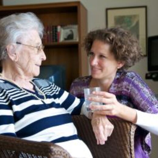Pflegepersonal reicht einer Seniorin ein Glas Wasser