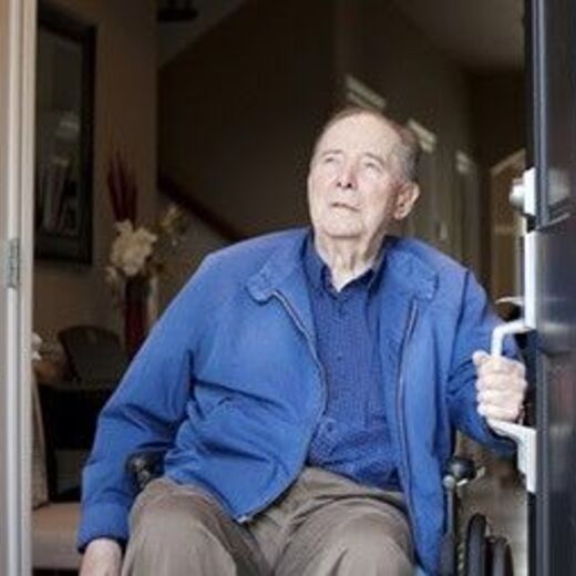 Senior im Rollstuhl steht an Haustür und schaut nach draußen