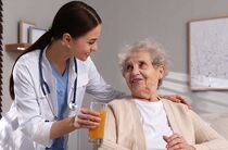 Den richtigen Pflegedienst suchen und finden: Eine Pflegerin bringt einem älteren Mann ein Tablett mit Essen und Trinken